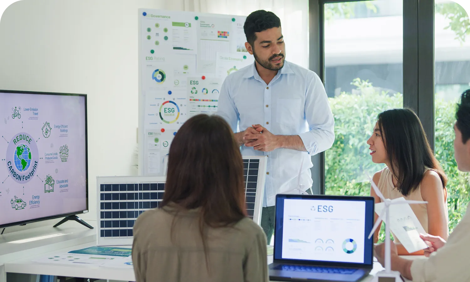 Grayson Risk Consulting A man presents ESG data on a screen to three colleagues in a meeting room, with laptops and printed materials displayed around a table.